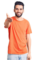 Naklejka premium Young handsome man with beard wearing casual t-shirt smiling friendly offering handshake as greeting and welcoming. successful business.