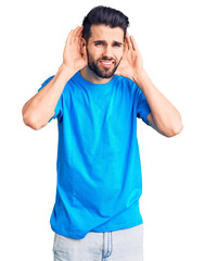 Young handsome man with beard wearing casual t-shirt trying to hear both hands on ear gesture, curious for gossip. hearing problem, deaf