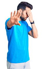 Young handsome man with beard wearing casual t-shirt covering eyes with hands and doing stop gesture with sad and fear expression. embarrassed and negative concept.