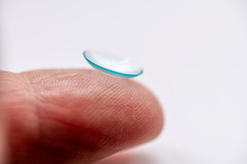 A macro side view of a eye contact lens on the tip of a finger isolated in a white background.