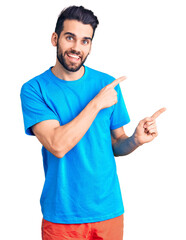 Young handsome man with beard wearing casual t-shirt smiling and looking at the camera pointing with two hands and fingers to the side.