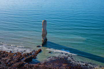 Chalk or limestone cliffs and natural arches and a pointed formation called L'Aiguille (aiguille de Belval) along the English Channel near Étretat, Normandy, France. Seascape on a clear day.