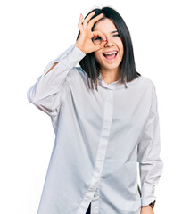 Young brunette woman with blue eyes wearing oversize white shirt doing ok gesture with hand smiling, eye looking through fingers with happy face.