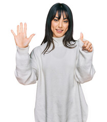 Young brunette woman with bangs wearing casual turtleneck sweater showing and pointing up with...