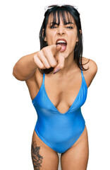 Young hispanic woman wearing swimsuit and sunglasses pointing displeased and frustrated to the camera, angry and furious with you