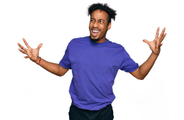 Young african american man with beard wearing casual purple t shirt crazy and mad shouting and yelling with aggressive expression and arms raised. frustration concept.