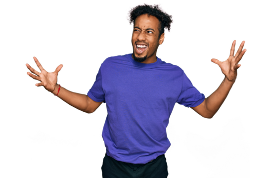 Young african american man with beard wearing casual purple t shirt crazy and mad shouting and yelling with aggressive expression and arms raised. frustration concept.