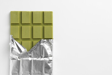 Tasty matcha chocolate bar wrapped in foil on white background, top view. Space for text