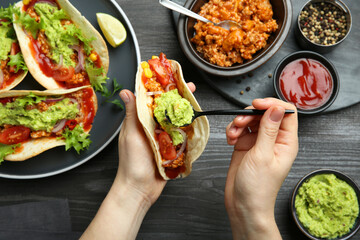 Woman adding guacamole to delicious taco at wooden table, top view