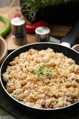 Fried ground meat in frying pan and microgreens on table, closeup