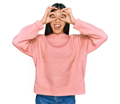 Beautiful young asian woman wearing casual winter sweater doing ok gesture like binoculars sticking tongue out, eyes looking through fingers. crazy expression.