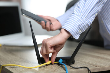 Woman with smartphone connecting cable to Wi-Fi router at wooden table indoors, closeup