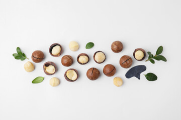 Tasty Macadamia nuts and green leaves on white background, flat lay