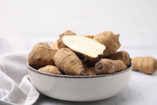 Whole and cut tubers of turnip rooted chervil in bowl on white tiled table, closeup