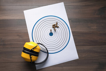 Shooting target, headphones and bullets on wooden table, top view