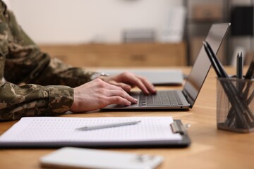 Military service. Soldier working with laptop at wooden table indoors, closeup - obrazy, fototapety, plakaty