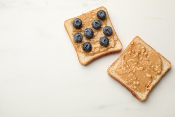 Delicious toasts with peanut butter and blueberries on white marble table, flat lay. Space for text