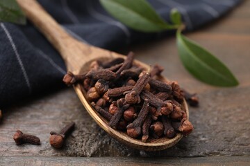 Spoon with aromatic cloves on wooden table, closeup