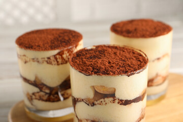 Delicious tiramisu in glasses on blurred background, closeup