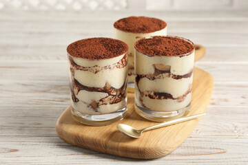 Delicious tiramisu in glasses and spoon on light wooden table