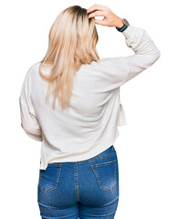 Young caucasian woman wearing casual winter sweater backwards thinking about doubt with hand on head