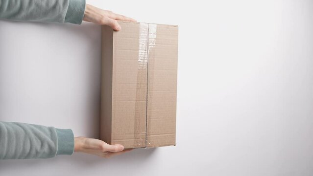 Unpacking carton box on white background. Female hands put box on table, cut mail box with clerical knife, unpacking postal package. Woman open new parcel. Receiver unzip post pack. View from above
