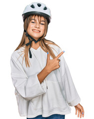 Teenager caucasian girl wearing bike helmet cheerful with a smile of face pointing with hand and finger up to the side with happy and natural expression on face