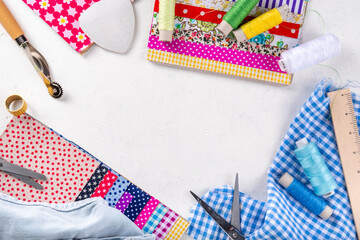 Fototapeta premium Sewing, needlework and clothing repair, background, scrapbooking, quilting. Colorful pieces of fabric, scissors, ruler, sewing tools, needles, threads on a white table background top view copy space