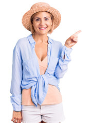 Young blonde woman wearing summer hat smiling happy pointing with hand and finger to the side