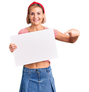 Young blonde woman holding blank empty banner smiling happy pointing with hand and finger