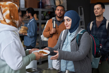 Waist up portrait of adult Middle Eastern woman wearing hijab taking hot meal at refugee help center