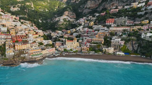 Flying above colorful houses, church and beach with turquoise water - Positano village, Italy. Famous tourist resort of the Amalfi coast - Positano. UHD, 4K