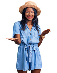 Young indian girl wearing summer hat smiling cheerful with open arms as friendly welcome, positive and confident greetings