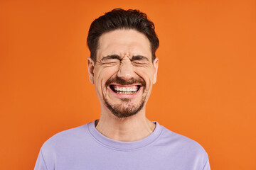 happiness, excited bearded man in purple sweatshirt smiling with closed eyes on orange background