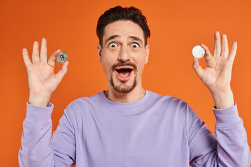 amazed bearded man holding bitcoins in his hands and smiling on orange background, cryptocurrency