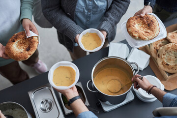 High angle closeup of volunteers hands giving out free food to Middle Eastern refugees at soup kitchen, copy space