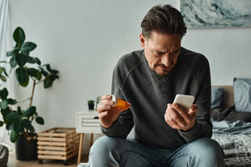 confused bearded man reading prescription o his smartphone while holding bottle with pills - obrazy, fototapety, plakaty