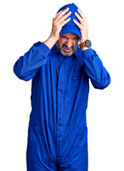 Middle age handsome man wearing mechanic uniform suffering from headache desperate and stressed because pain and migraine. hands on head.