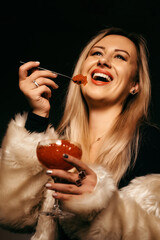 Beautiful blonde girl eats red caviar with a spoon