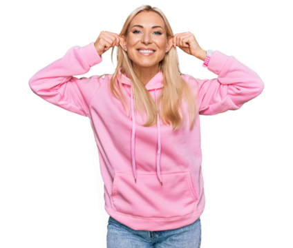 Young blonde woman wearing casual sweatshirt smiling pulling ears with fingers, funny gesture. audition problem