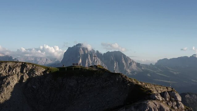 Aerial view Italian Dolomites Seceda, cross and people on the summit, scenic clouds in the background