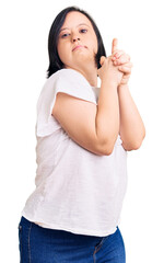 Brunette woman with down syndrome wearing casual white tshirt holding symbolic gun with hand gesture, playing killing shooting weapons, angry face