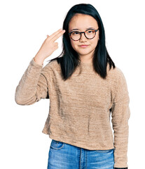 Young chinese woman wearing casual sweater and glasses shooting and killing oneself pointing hand and fingers to head like gun, suicide gesture.