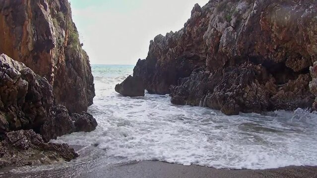 Choppy sea on the small beach in the rocky cove between two jagged cliffs. Marina di Camerota, Salerno, Italy.