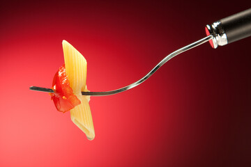Fork with pasta and tomato on a red background