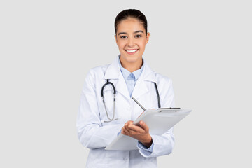 Happy millennial caucasian lady doctor white coat make notes at clipboard