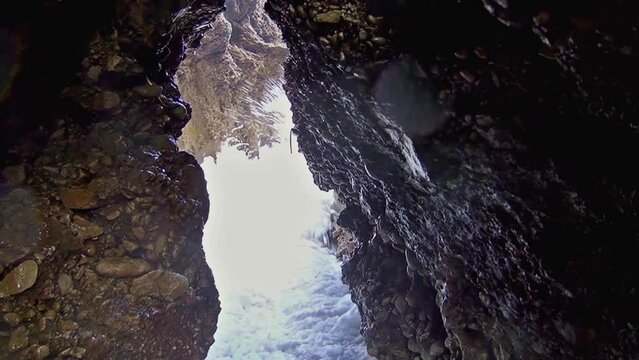 Camera quickly retreating between rocks in cliff tunnel due to the force of sea waves.