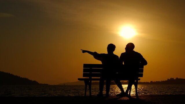 Couple in love on bench in colorful dusk. A view of silhouette of couple in love resting on bench by the lake during holiday time.