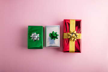 Creative handmade christmas green, red and silver shiny gift boxes with decor on pastel pink background, top view.