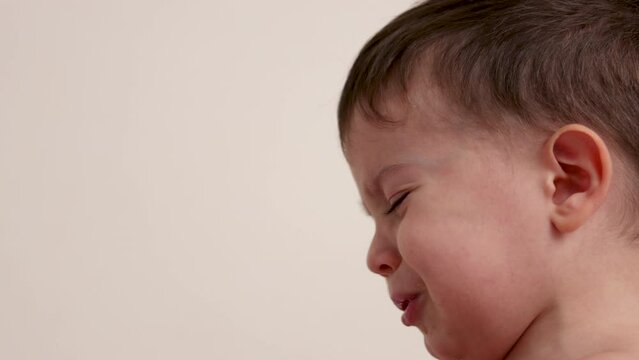 cute baby boy is upset,making air and graces,whims. lying kid child is crying.child walking in room or sitting on blanket.boy rubbing eyes with hand, finger in nose hole. maternity leave concept 